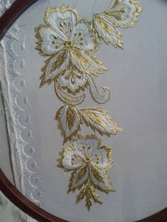 an embroidered piece of cloth with gold and white flowers on it in a wooden frame