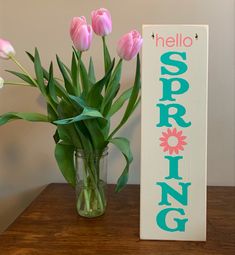 pink tulips are in a vase next to a sign that says hello spring