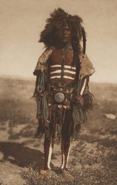 an old photo of a native american man in the desert with feathers on his head