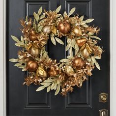 a wreath is hanging on the front door with gold and green ornaments around it's edges