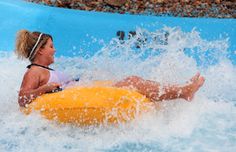 a woman riding on top of an inflatable raft down a wave pool at a water park