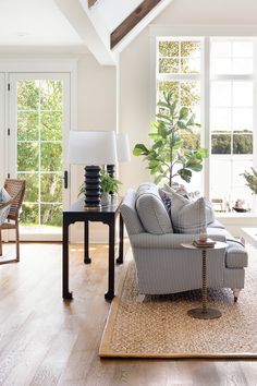 a living room filled with furniture and a large window covered in plants on top of a hard wood floor