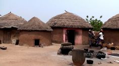 some people are standing in front of small huts with thatched roofs and pots on the ground