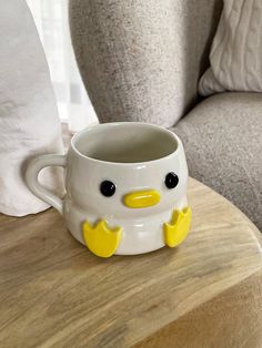 a coffee cup with a yellow beak sitting on top of a wooden table next to a gray chair