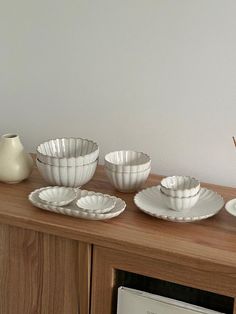 a wooden table topped with white dishes on top of it's sideboard next to a vase