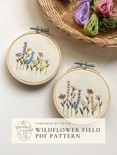 two embroidery hoops with flowers on them sitting next to a basket full of yarn