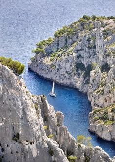 there is a boat that is in the water near some rocks and trees on the shore