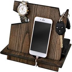 a cell phone is plugged in to a wooden stand with keys and watch on it