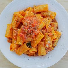 a white bowl filled with pasta covered in sauce and seasoning sitting on top of a wooden table