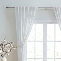 a vase filled with flowers on top of a wooden table next to a window covered in white curtains