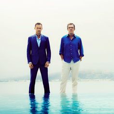 two men in blue shirts and white pants standing next to each other near the water