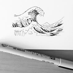 a drawing of an ocean wave on paper next to a pen and inking pad