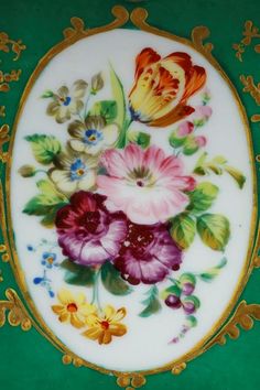 a plate with flowers painted on it and gold trimming around the edge, sitting on a green surface