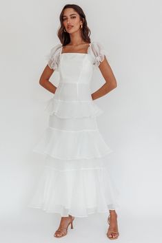 a woman wearing a white dress with tiered ruffles on the bottom and shoulders