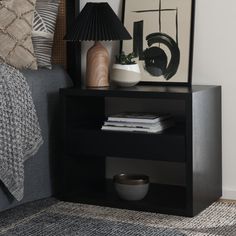 a nightstand with a lamp and pictures on the wall above it in a room that has carpeted flooring