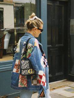 a woman walking down the street wearing a jean jacket with patchwork and patches on it