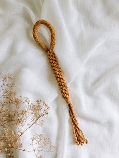 a piece of rope on top of a bed next to dried flowers and branches in front of a white sheet