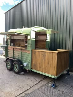 an old green trailer is parked in front of a building with a awning on it