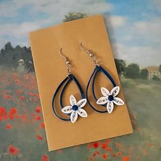 a pair of blue and white flower earrings on top of a piece of brown paper