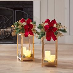 two lighted candles with red bows and greenery in them on the floor next to a fireplace