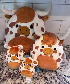 three stuffed animals sitting next to each other on top of a marble counter with white tiles behind them