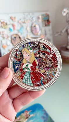 a hand holding a compact mirror with an image of princesses on it in front of a wall