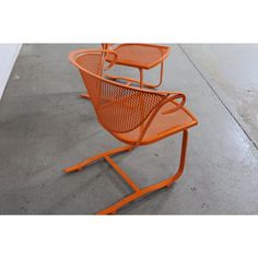 two orange chairs sitting next to each other on top of cement floored area with white walls