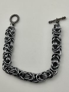 This byzantine rope chain bracelet is simple in its design. It is also lightweight, and holds up well. The design is such that it would look good on a large or small wrist size, just be sure to specify the desired length in the personalization options. This is annodized aluminum, making it lightweight, and the black ice color gives it a hint of blue or purple in the right lighting. Charms can be added - message me to start a custom order. Everyday Silver Metal Braided Bracelets, Silver Metal Box Chain Bracelet, Metal Link Bracelets With Jump Ring, Silver Link Bracelet With Jump Ring, Handmade Metal Chain Bracelet With Rectangular Links, Handmade Chain Bracelet With Rectangular Metal Links, Brutalist Design, Bracelets Design, Design Bracelet