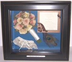 a shadow box frame with flowers, feathers and a vase in it on a table