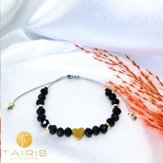 a black beaded bracelet with gold hearts on it and an orange flower next to it