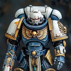 a blue and gold painted warhammer with wings on it's chest, standing in front of a black background