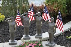 four statues with american flags on them in front of flowers and bushes, one is holding an american flag