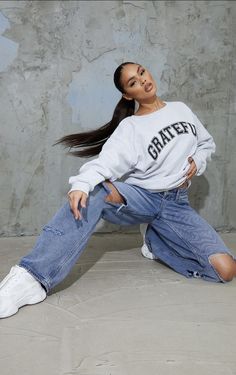 a woman sitting on the ground with her legs crossed wearing jeans and a white sweatshirt