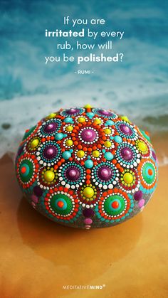 a colorful rock sitting on top of a sandy beach next to the ocean with a quote from rumi