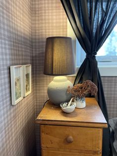 a table with a lamp and vase on it next to a window in a room