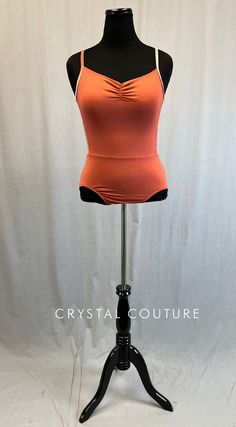 a mannequin wearing an orange top on a black stand