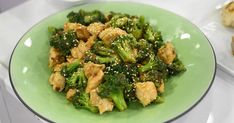 a green plate topped with chicken and broccoli covered in sesame seed flakes