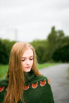 a woman with long red hair wearing a green sweater looking down at her cell phone