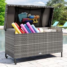 an outdoor wicker storage box filled with different colored items next to a swimming pool