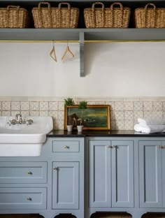 a kitchen with blue cabinets and baskets on the shelves above it, along with a white sink