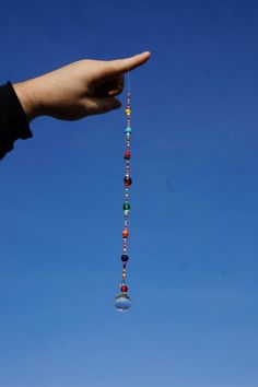 a hand holding a beaded necklace in front of a clear blue sky with clouds