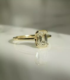 a yellow gold ring with an emerald cut diamond in the center on a white surface