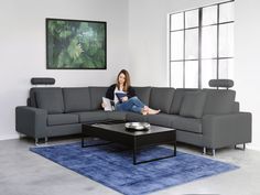 a woman sitting on top of a gray couch next to a blue rug in a living room