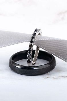 two black rings with white diamonds on them sitting next to a gray ribbon and grey fabric