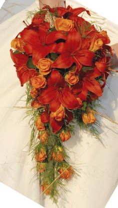 a bridal bouquet with orange flowers and greenery on the bride's arm