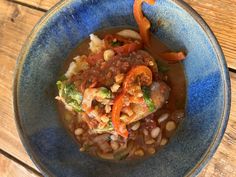 a blue bowl filled with beans and vegetables on top of a wooden table next to a spoon