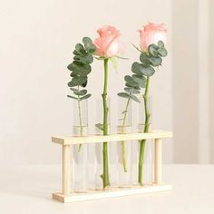 three vases with pink roses in them on a white counter top, one is holding green leaves