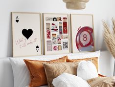 a bed topped with lots of pillows next to two pictures on the wall above it