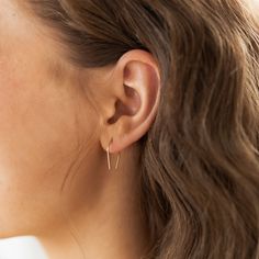 a close up of a woman's ear wearing small gold hoop earrings and a white shirt