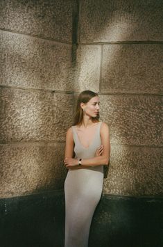 a woman standing in front of a wall with her arms crossed and looking off to the side